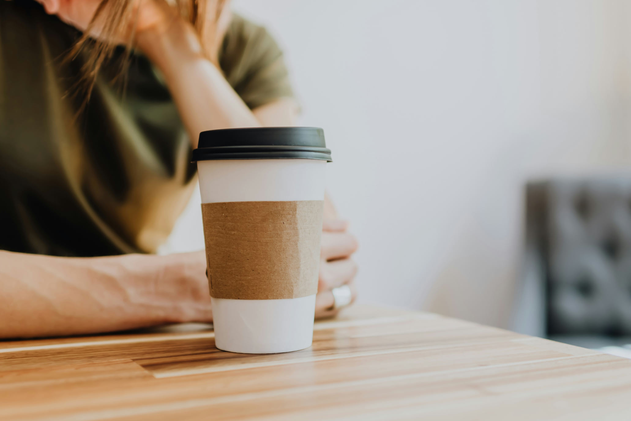 A person drinks a coffee sitting up to a table